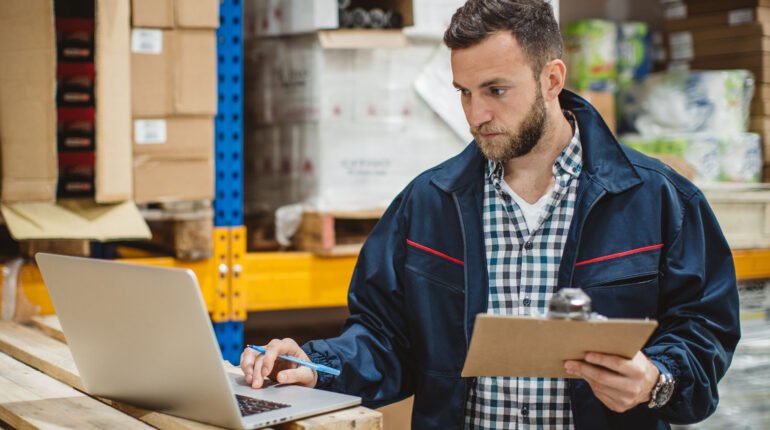 Distribution workers working in warehouse. They checking merchandise on laptop and collecting information about inventory